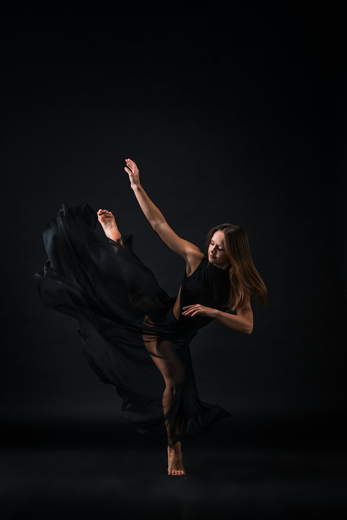 Young beautiful dancer in beige dress dancing on black background
